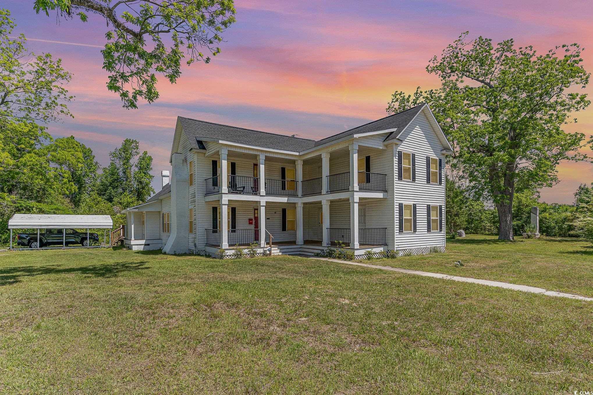 Neoclassical / greek revival house featuring covered porch, a yard, a balcony, and a detached carport