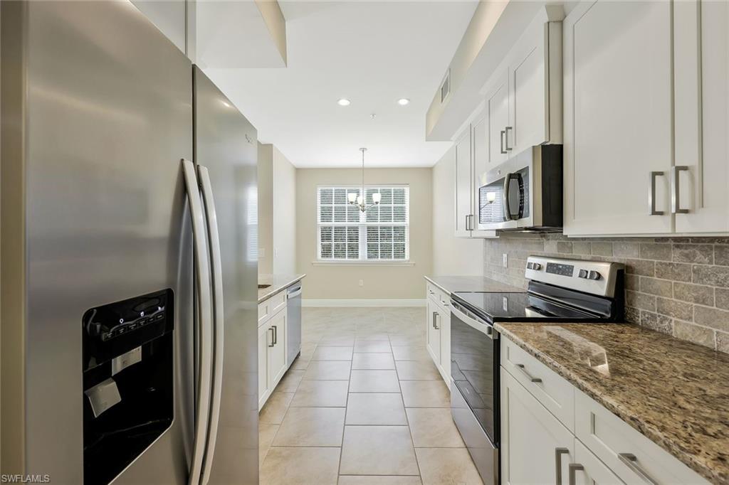 18225 Creekside Preserve Loop, Unit 102 Fort Myers, FL 33908 - Photo 12 of 25 Kitchen featuring appliances with stainless steel finishes, white cabinetry, light tile patterned floors, light stone counters, and backsplash