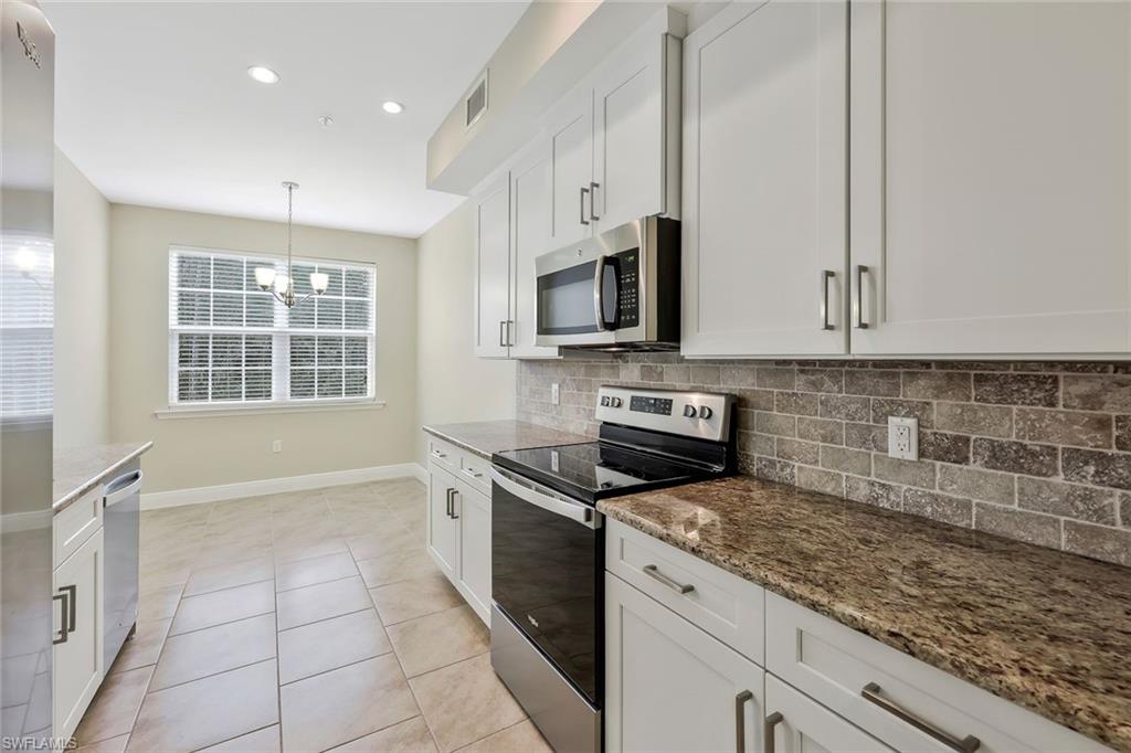 18225 Creekside Preserve Loop, Unit 102 Fort Myers, FL 33908 - Photo 13 of 25 Kitchen featuring appliances with stainless steel finishes, white cabinetry, light tile patterned floors, hanging light fixtures, and decorative backsplash