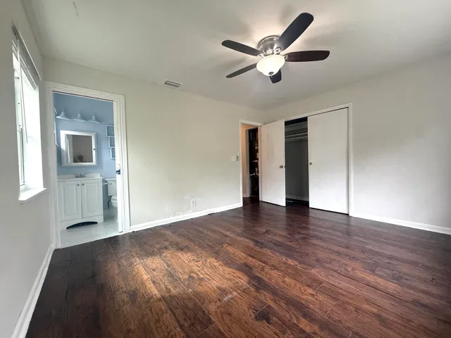 a view of an empty room with wooden floor and a ceiling fan