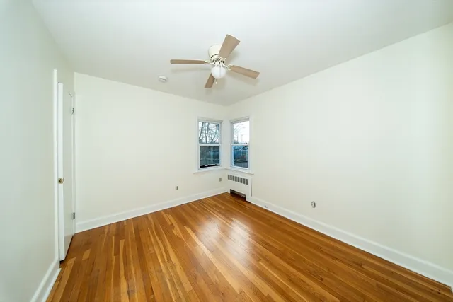 an empty room with wooden floor ceiling fan and windows