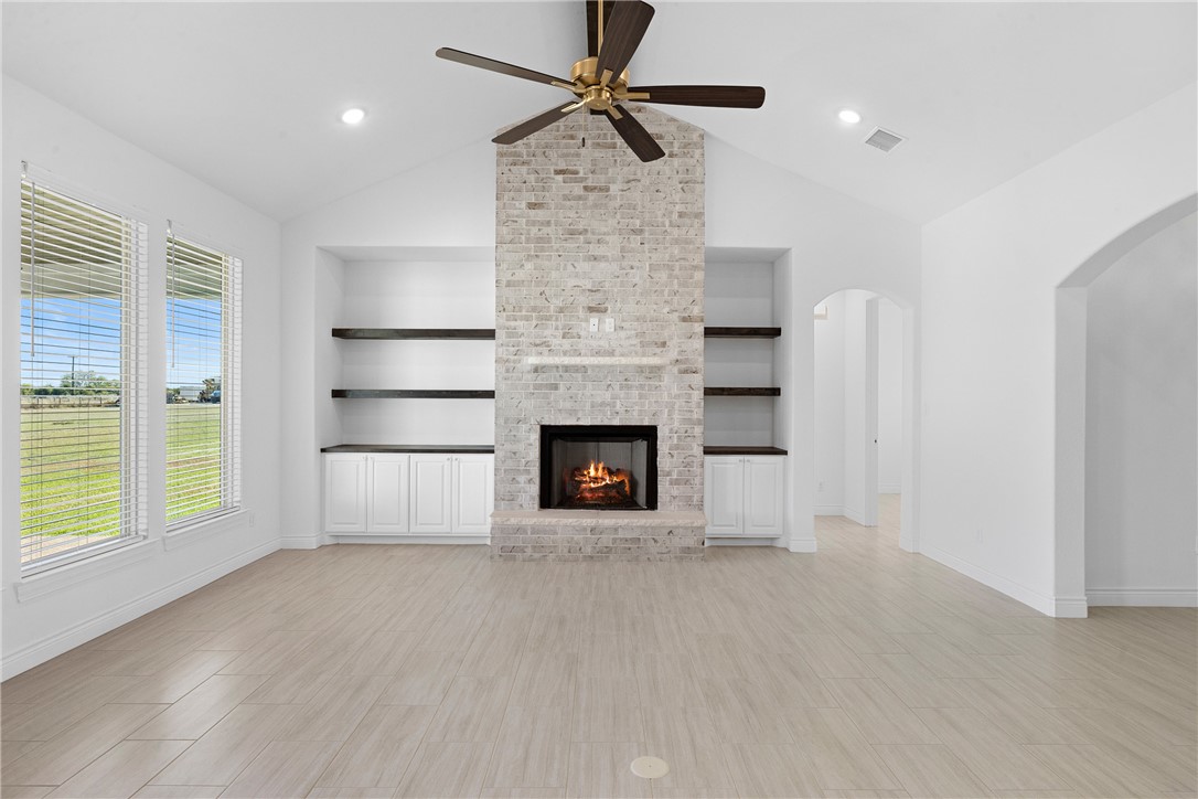 6524 Agave Court Bryan, TX 77808 - Photo 16 of 43 Unfurnished living room with wood finish floors, lofted ceiling, a brick fireplace, a ceiling fan, and built in features