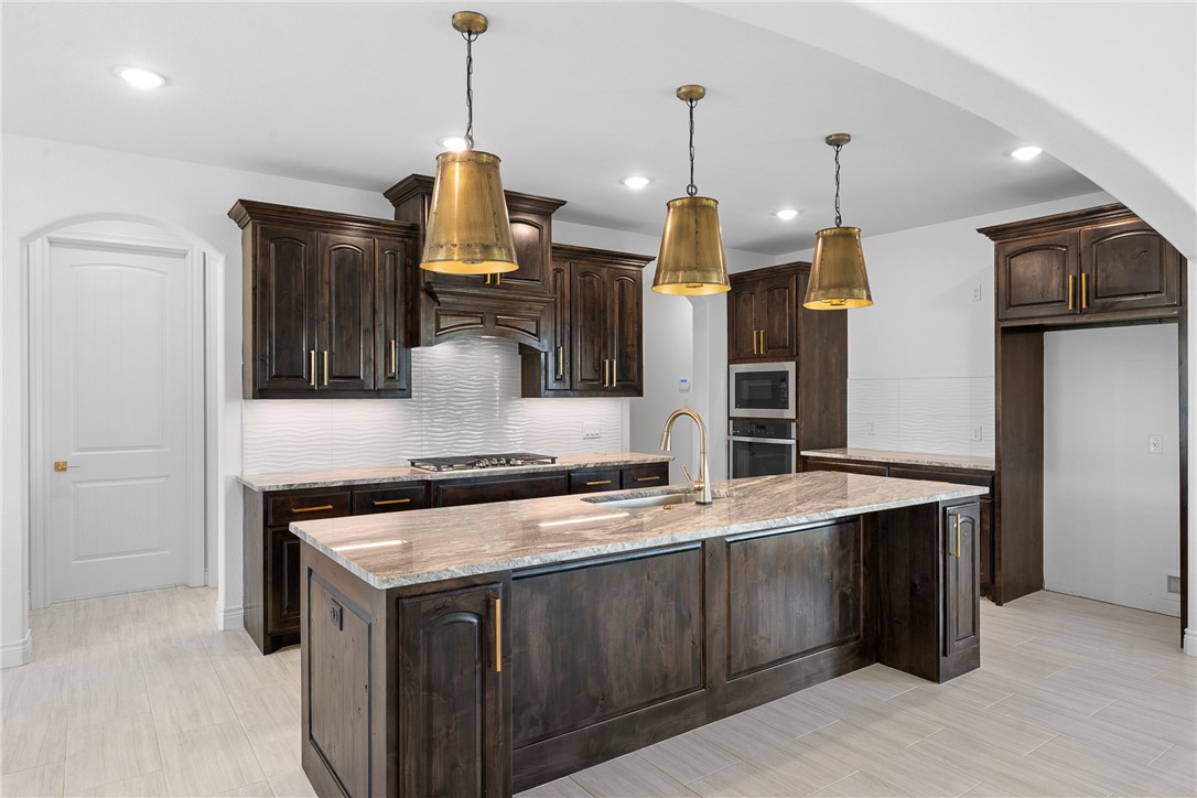 6524 Agave Court Bryan, TX 77808 - Photo 17 of 43 Kitchen featuring dark brown cabinets, backsplash, arched walkways, light stone countertops, and pendant lighting
