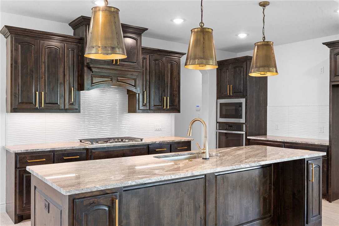 6524 Agave Court Bryan, TX 77808 - Photo 18 of 43 Kitchen featuring decorative backsplash, dark brown cabinetry, light stone countertops, a kitchen island with sink, and appliances with stainless steel finishes