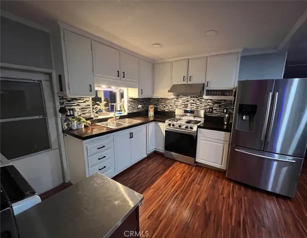 a kitchen with stainless steel appliances granite countertop a refrigerator a sink dishwasher a stove and white countertops with wooden floor