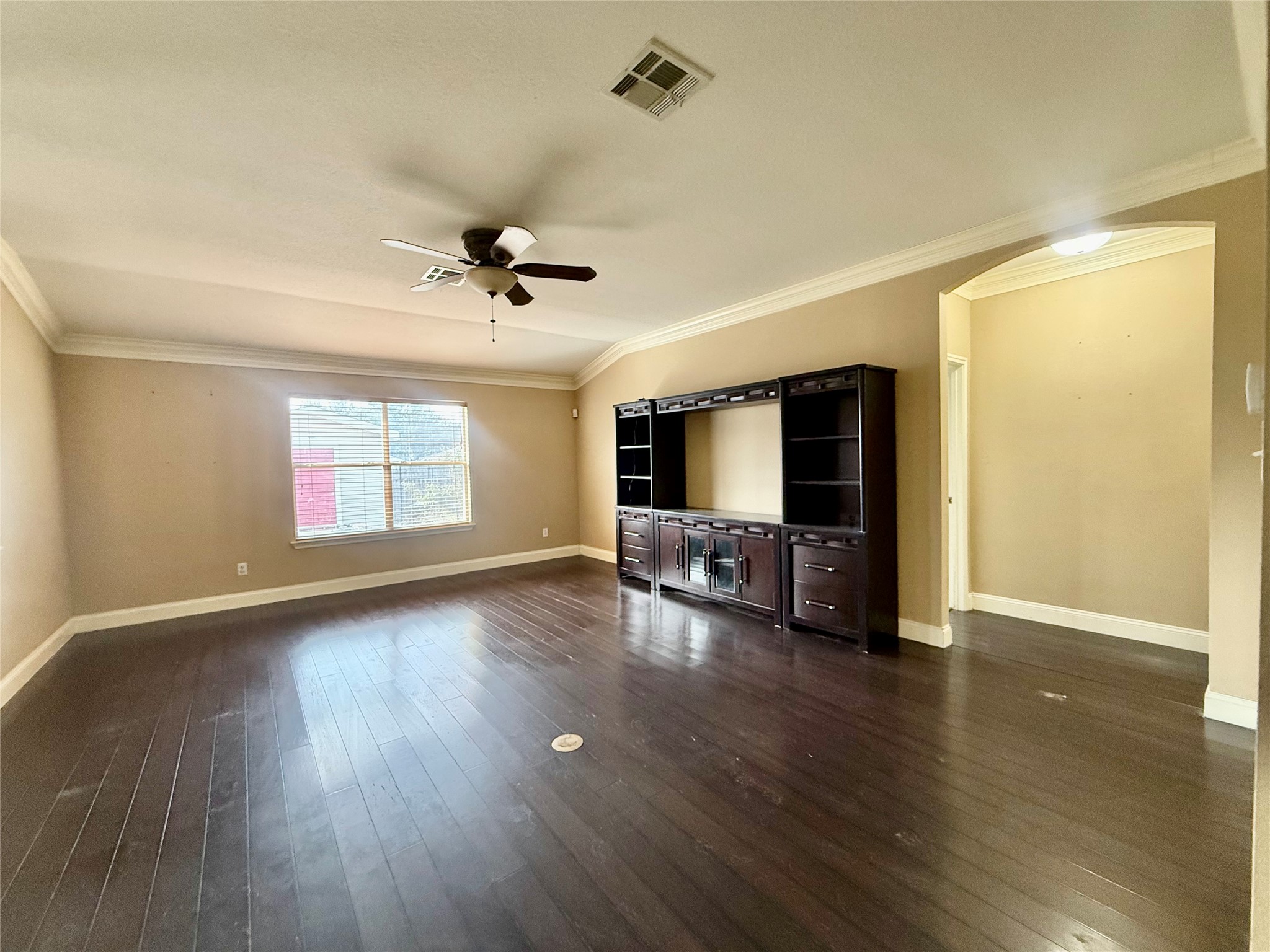 12820 Waynespur Lane Elgin, TX 78621 - Photo 7 of 26 Unfurnished living room featuring dark wood-style flooring, crown molding, a ceiling fan, and arched walkways