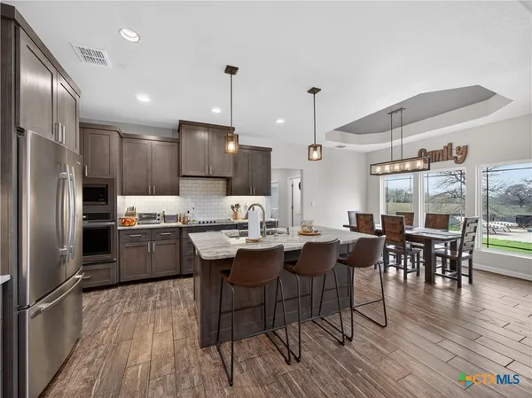a kitchen with stainless steel appliances a dining table chairs stove refrigerator and wooden floor