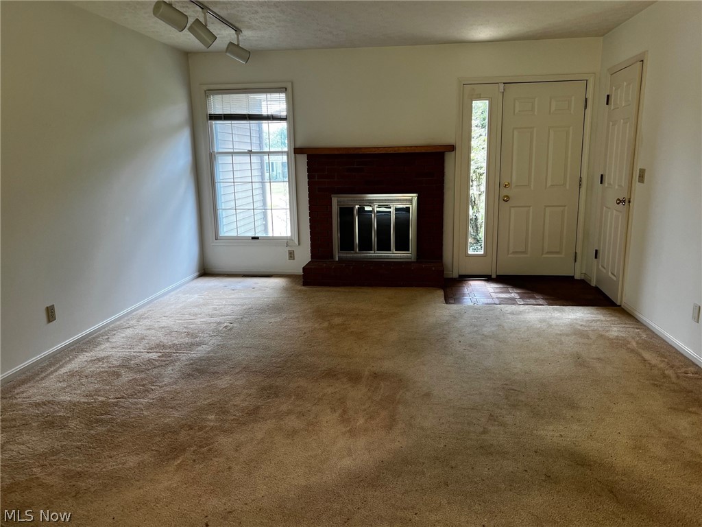 Unfurnished living room featuring a textured ceiling, dark colored carpet, a fireplace, and rail lighting