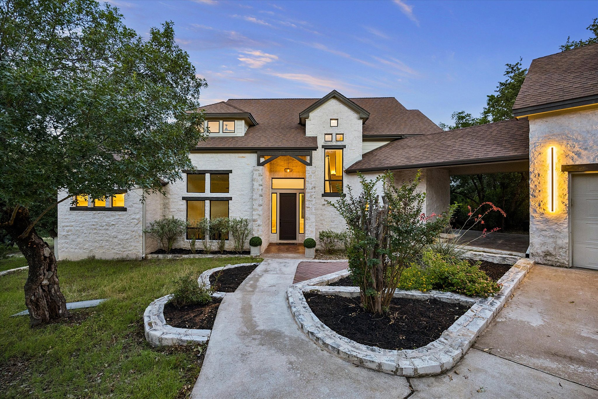 3719 Bee Creek Road Spicewood, TX 78669 - Photo 1 of 40 A striking contemporary residence with warm lighting highlights the textured stone facade and well-maintained landscaping.