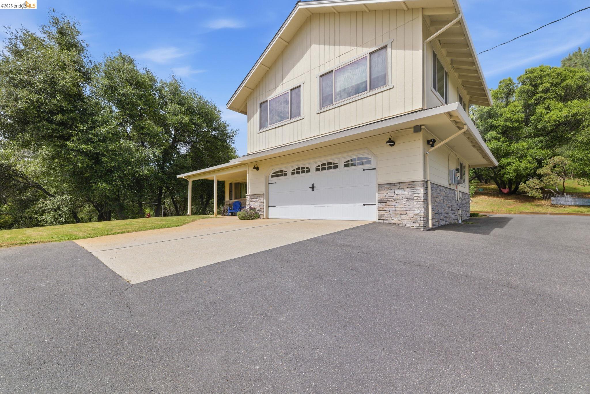 16860 Buckhorn Mountain Road Sonora, CA 95370 - Photo 2 of 46 View of property exterior featuring an attached garage, driveway, stone siding, and a lawn