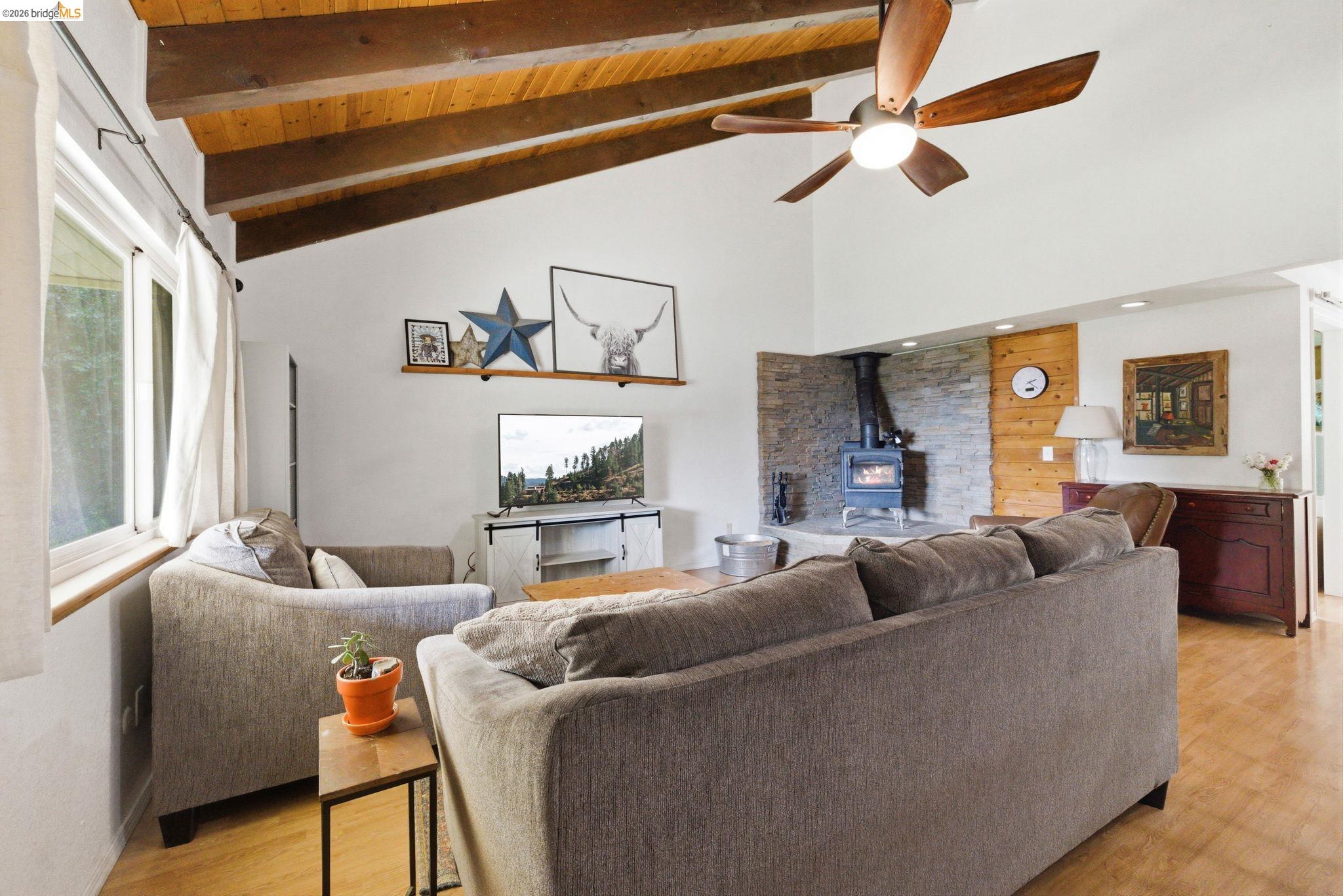 16860 Buckhorn Mountain Road Sonora, CA 95370 - Photo 22 of 46 Living area with a wood stove, a ceiling fan, light wood-style floors, and a high wood beamed ceiling