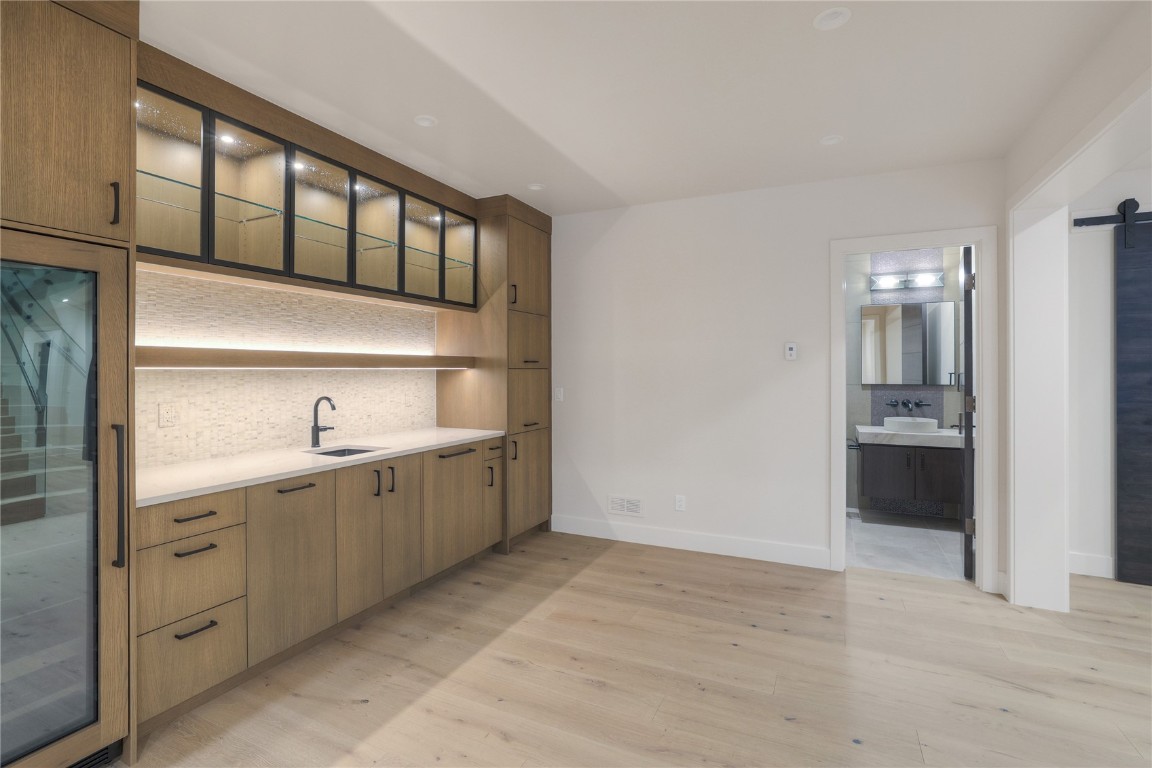 90 West Trade Court Keystone, CO 80435 - Photo 36 of 50 Kitchen featuring a barn door, light wood-style floors, beverage cooler, backsplash, and glass insert cabinets