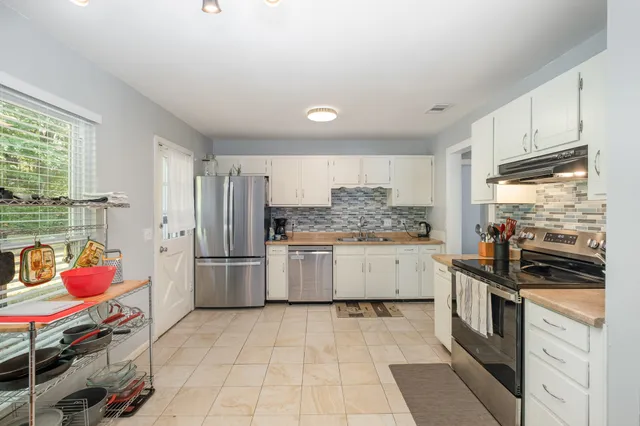 a kitchen that has a lot of white cabinets and stainless steel appliances