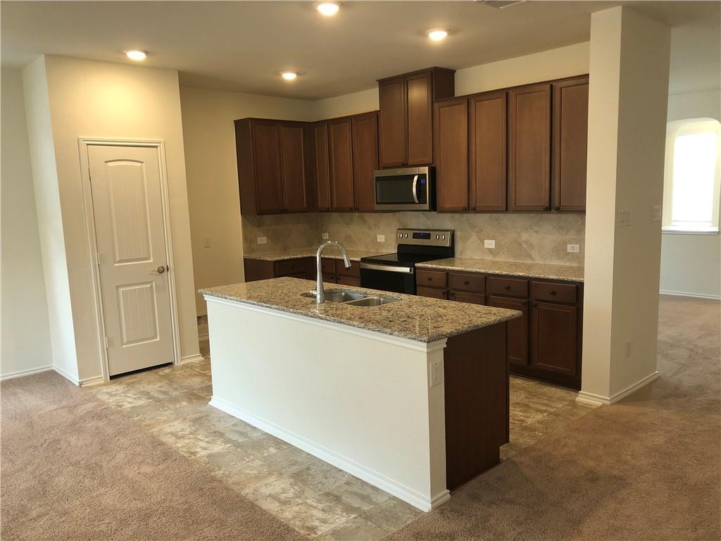 625 Jud Allen Way Leander, TX 78641 - Photo 6 of 18 Kitchen with light carpet, light stone countertops, stainless steel appliances, dark wood finish cabinets, and arched walkways