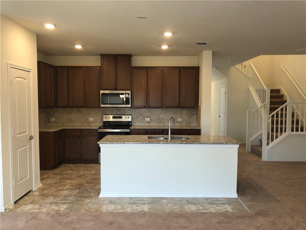 625 Jud Allen Way Leander, TX 78641 - Photo 7 of 18 Kitchen featuring dark wood finish cabinets, light stone counters, an island with sink, stainless steel appliances, and tasteful backsplash
