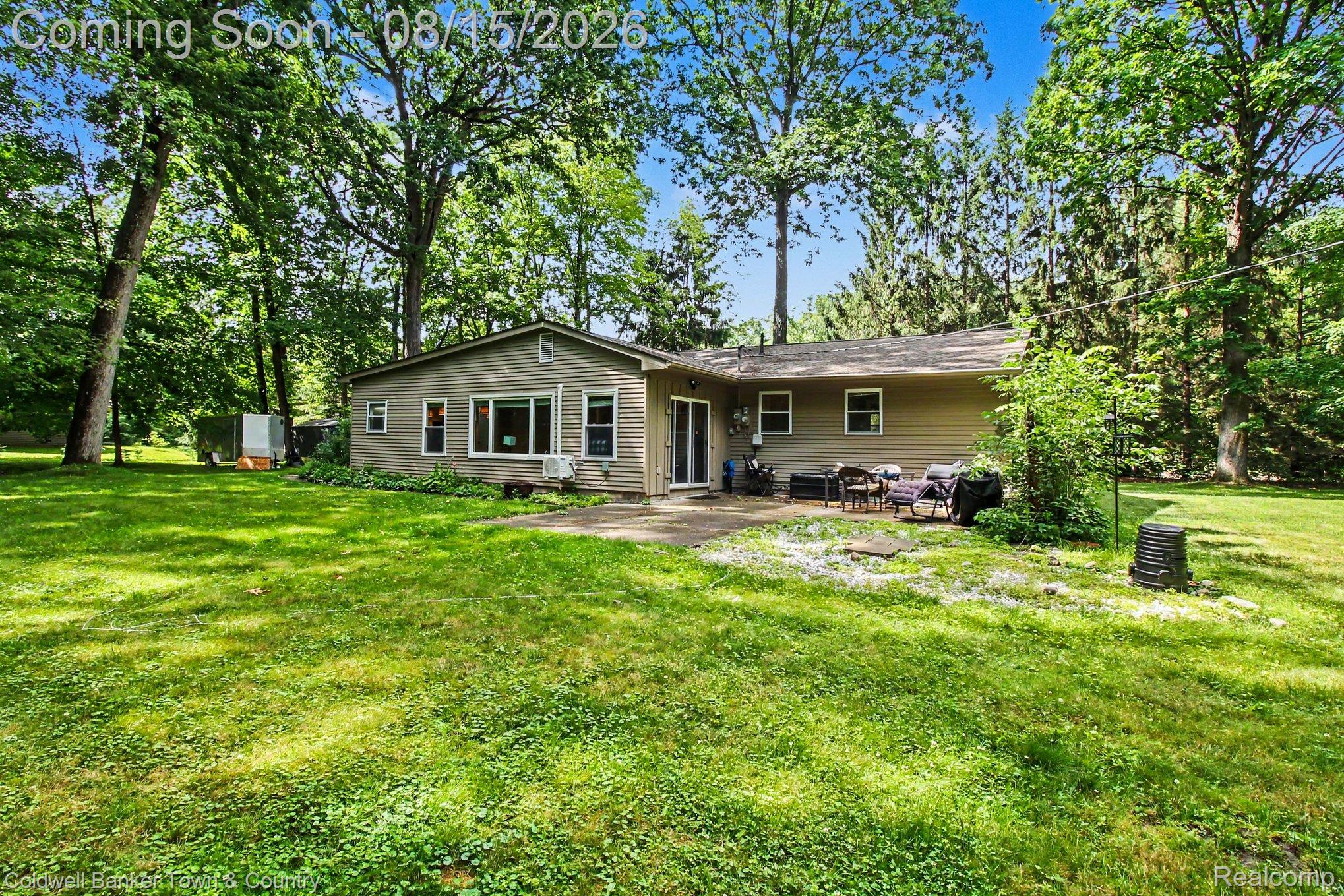 5444 Golf Club Road Howell, MI 48843 - Photo 20 of 29 Spacious green lawn with mature trees, a tan siding exterior, and a rear patio