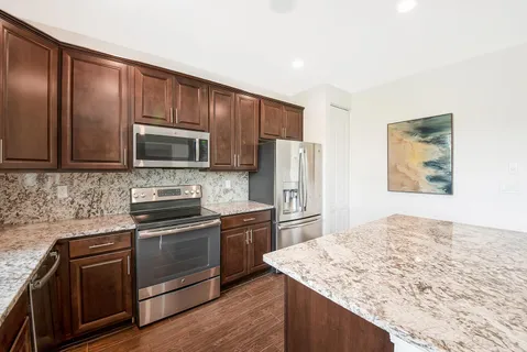 a kitchen with stainless steel appliances granite countertop a refrigerator a sink dishwasher a stove and white countertops with wooden floor