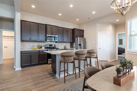 a kitchen with stainless steel appliances granite countertop a stove a refrigerator a sink a dining table and chairs with wooden floor