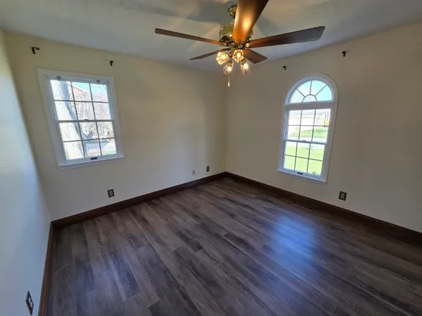 an empty room with wooden floor chandelier fan and windows