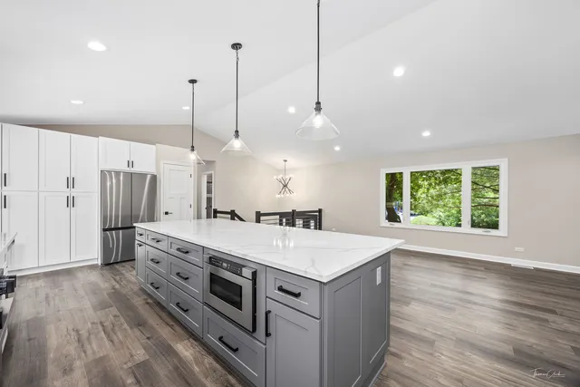 a kitchen with stainless steel appliances kitchen island granite countertop a sink a refrigerator a stove a kitchen island and chairs with wooden floor