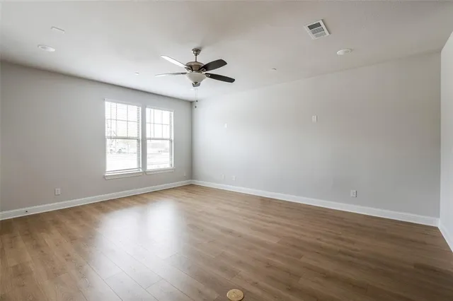 an empty room with wooden floor fan and windows