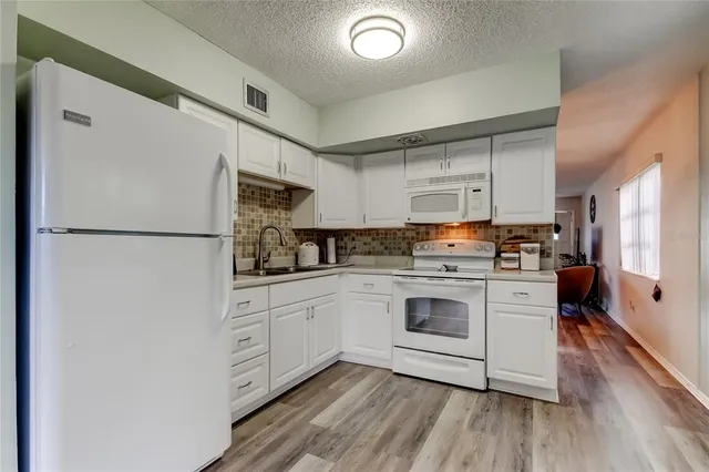 a kitchen with stainless steel appliances granite countertop a refrigerator a stove a sink and white cabinets