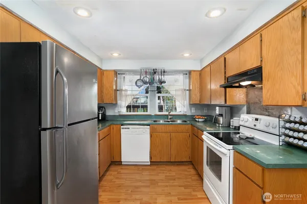 a kitchen with stainless steel appliances granite countertop a refrigerator a sink dishwasher a stove with wooden cabinets and floor