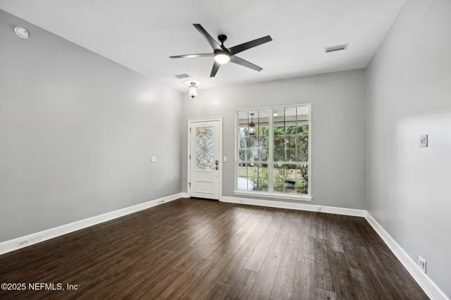 an empty room with wooden floor fan and windows