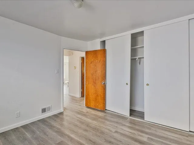 a view of an empty room with wooden floor and closet area