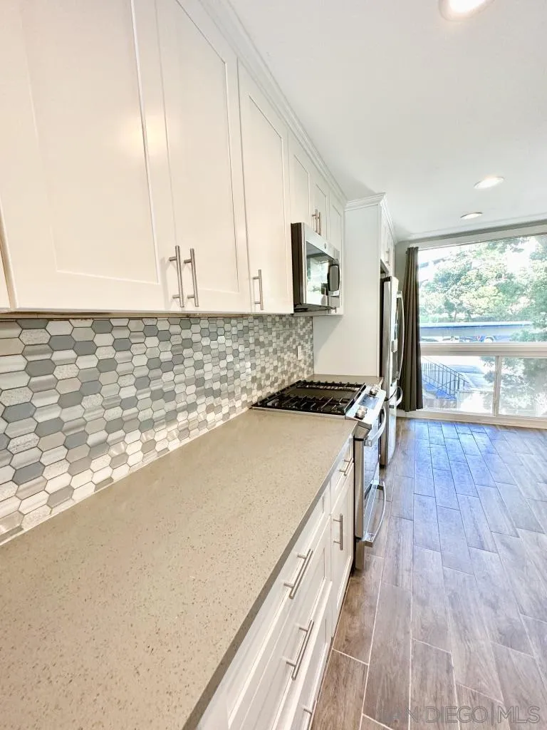 6855 Friars Road, Unit 14 San Diego, CA 92108 - Photo 14 of 31 a view of a kitchen with kitchen island a sink wooden floor and a large window