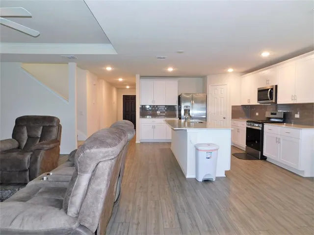 a large kitchen with stainless steel appliances granite countertop a large center island a stove a refrigerator a sink a dining table and chairs with wooden floor