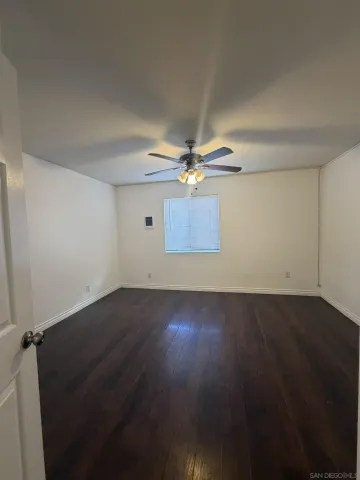 an empty room with wooden floor fan and windows