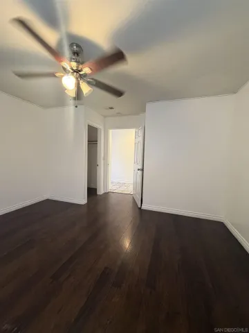 a view of an empty room with wooden floor and a ceiling fan