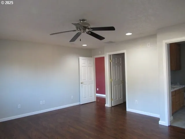 a view of an empty room with wooden floor and a ceiling fan