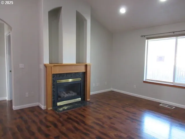 a view of an empty room with wooden floor and a fireplace