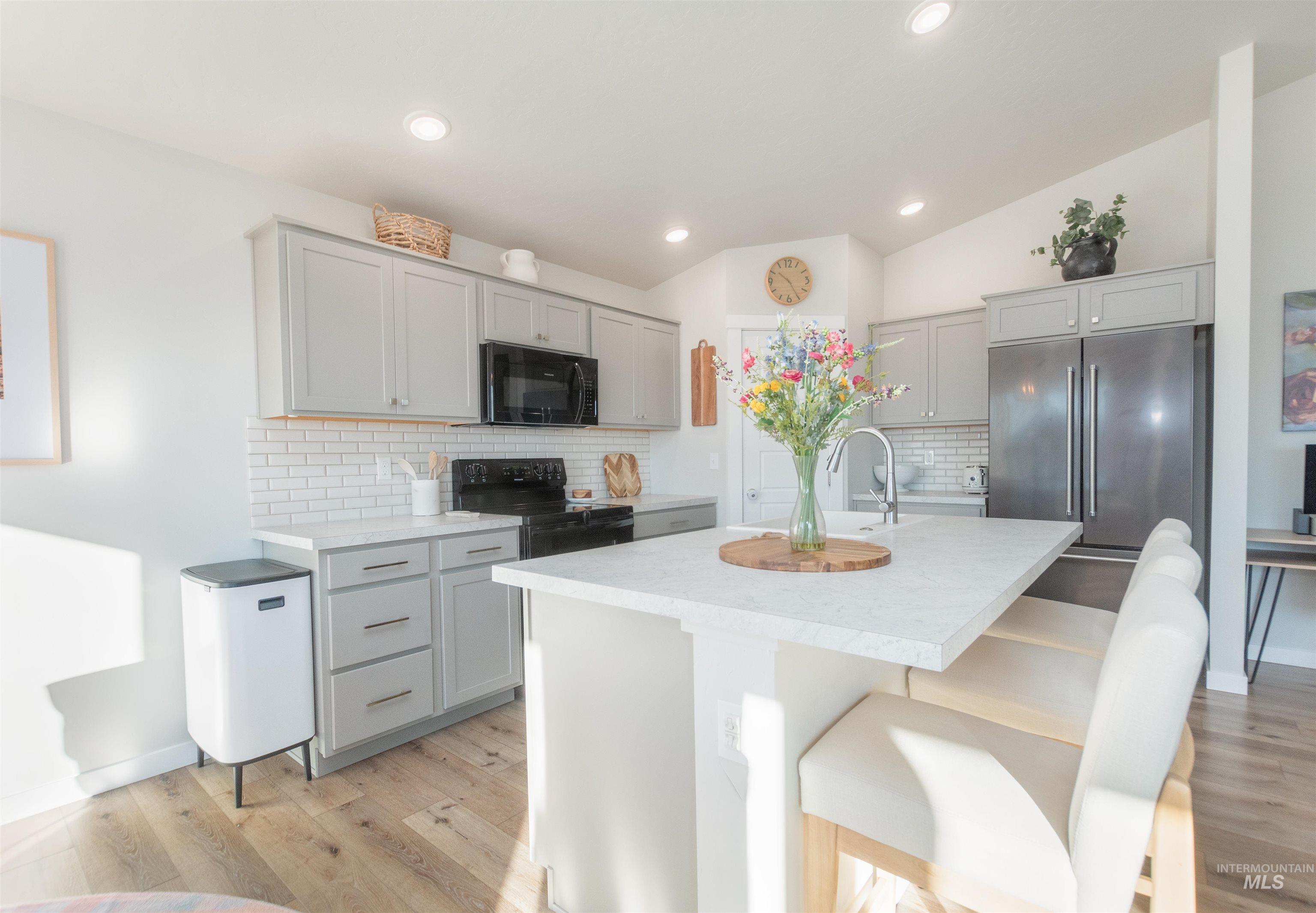 11289 West Langit Street Star, ID 83669 - Photo 10 of 33 Kitchen featuring gray cabinets, light countertops, light wood-style flooring, black appliances, and a kitchen breakfast bar