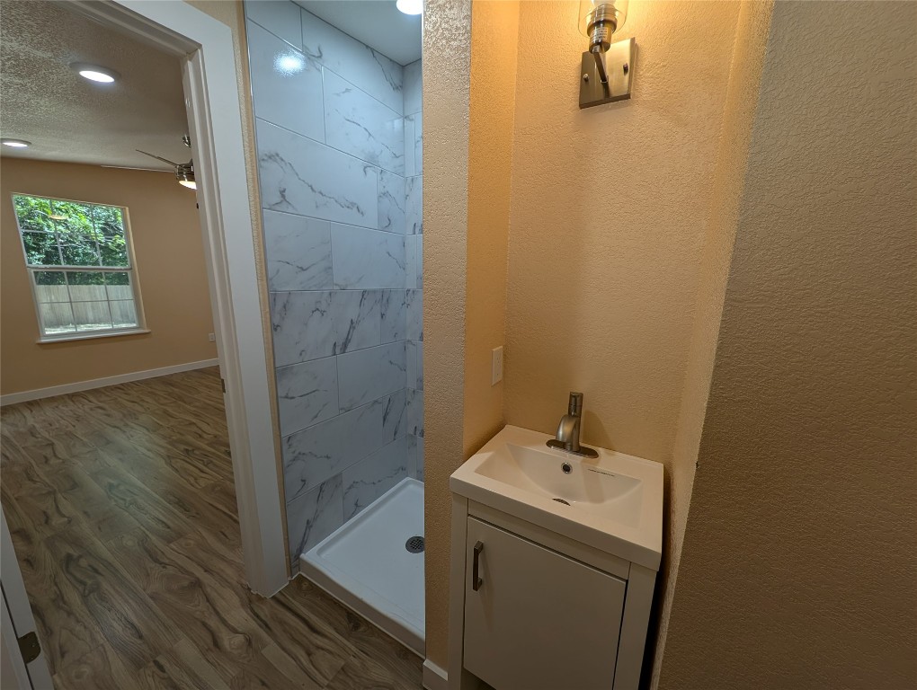 320 Laredo Street Lockhart, TX 78644 - Photo 12 of 27 Bathroom featuring wood finished floors, a stall shower, vanity, a ceiling fan, and a textured ceiling