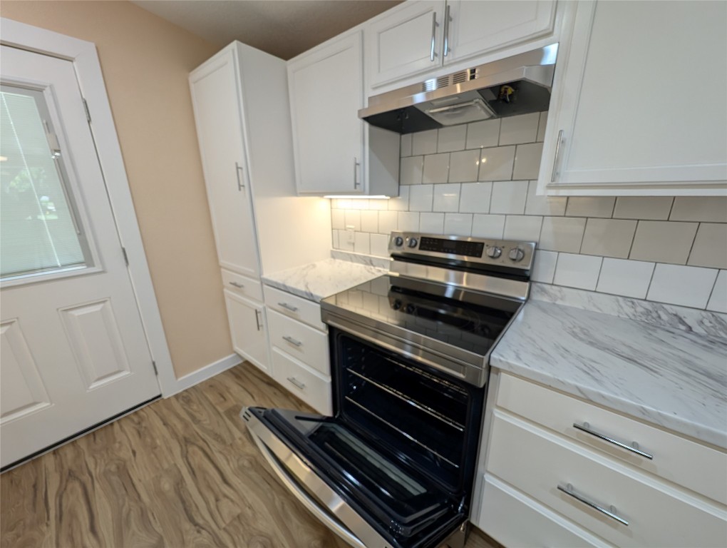 320 Laredo Street Lockhart, TX 78644 - Photo 6 of 27 Kitchen with under cabinet range hood, stainless steel electric stove, white cabinetry, dark wood-type flooring, and light stone counters