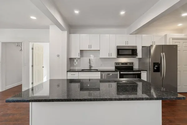 a kitchen with stainless steel appliances granite countertop a sink dishwasher a refrigerator and a stove with wooden floor