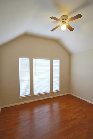 an empty room with wooden floor fan and windows