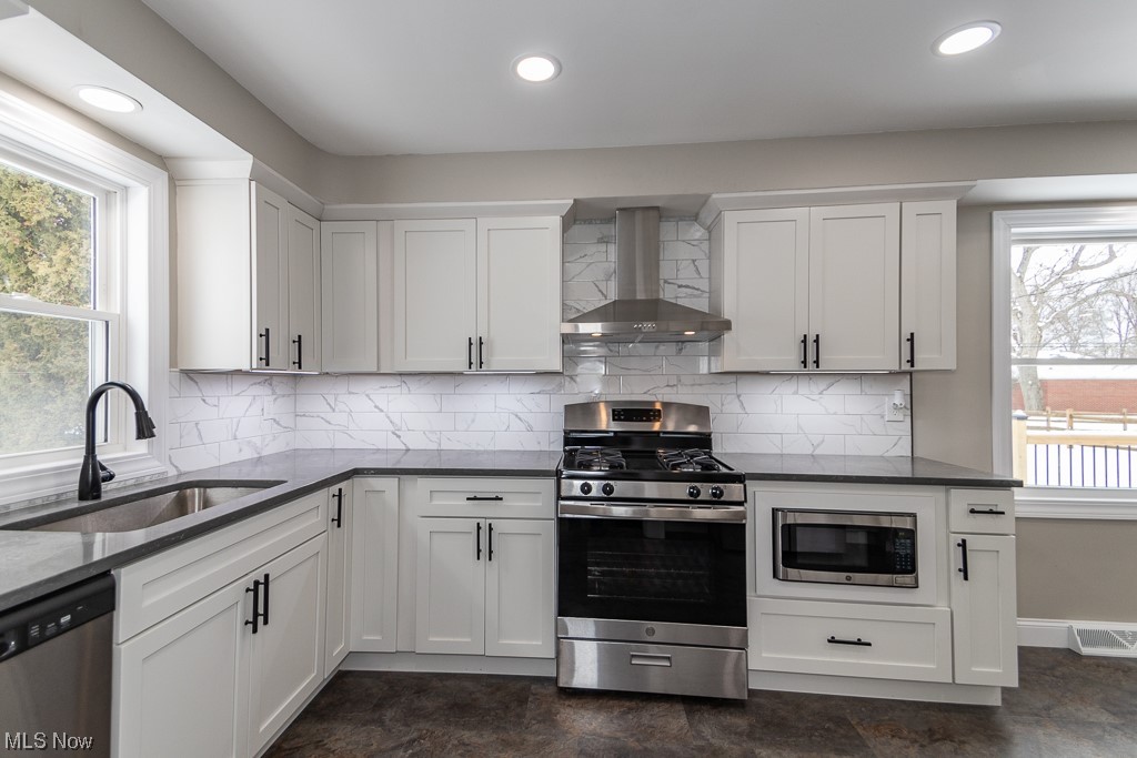 4980 Emmet Road Lyndhurst, OH 44124 - Photo 10 of 39 Kitchen with wall chimney range hood, white cabinets, appliances with stainless steel finishes, backsplash, and sink
