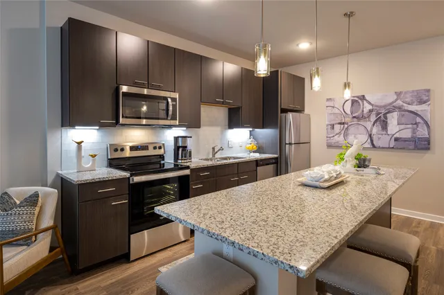 a kitchen with granite countertop kitchen island stainless steel appliances a sink stove and refrigerator