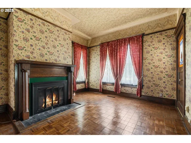 a view of an empty room with wooden floor fireplace and a window