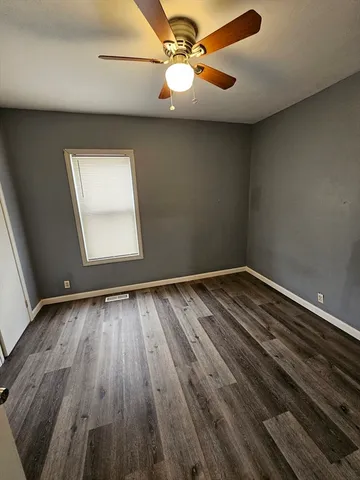 an empty room with wooden floor chandelier fan and windows
