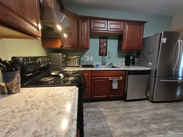 a kitchen with stainless steel appliances a refrigerator a sink a stove and wooden cabinets