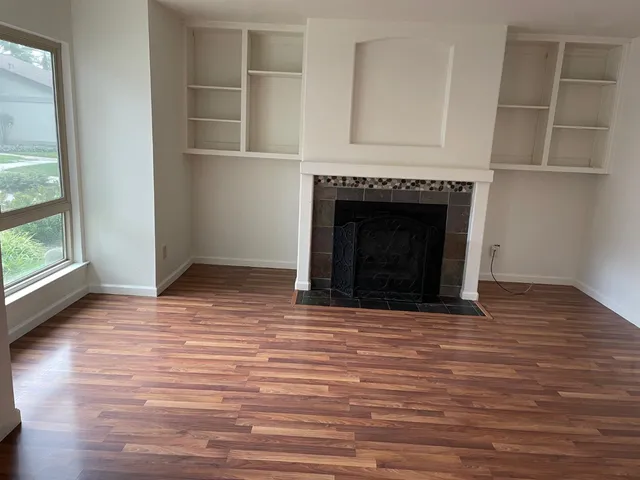 an empty room with wooden floor fireplace and windows