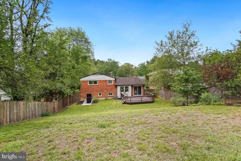 a house that is sitting in the grass with large trees and plants