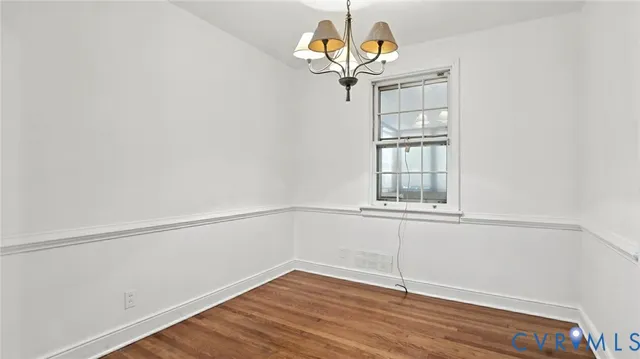 an empty room with wooden floor chandelier and windows