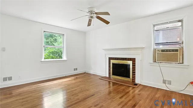 an empty room with windows a fireplace a ceiling fan and wooden floor