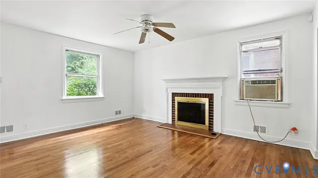a view of an empty room with wooden floor fireplace and a window